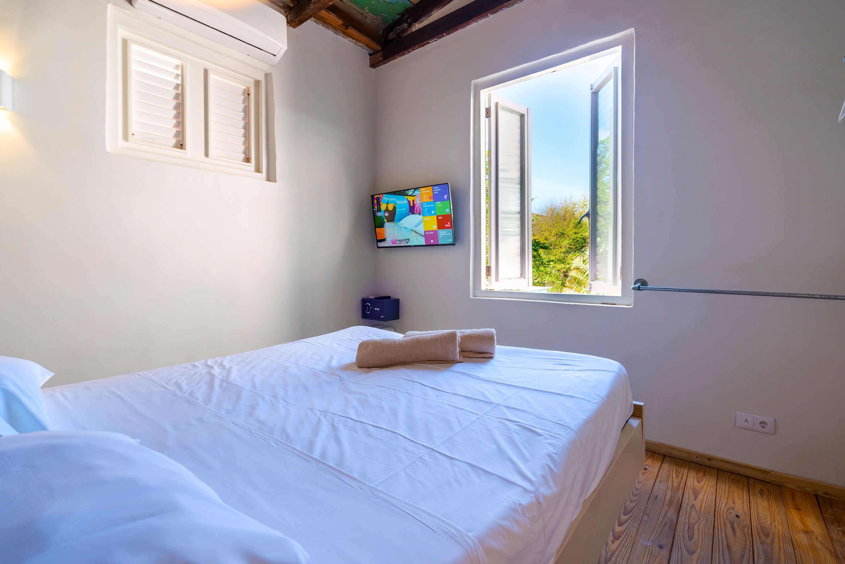 Un dormitorio con cama, ventana, televisor montado en la pared y radiador.