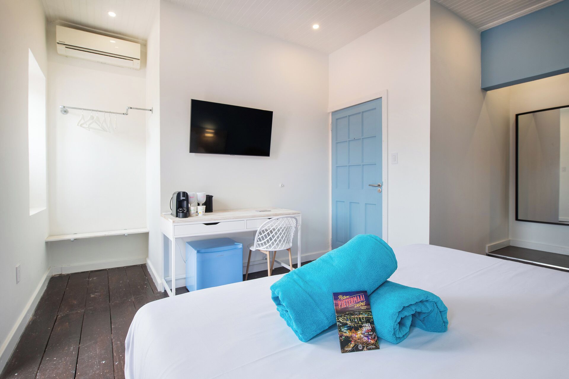 Een hotelkamer met een bed, bureau, stoel, televisie en een blauwe deur.