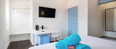 Een hotelkamer met een bed, bureau, stoel, televisie en een blauwe deur.