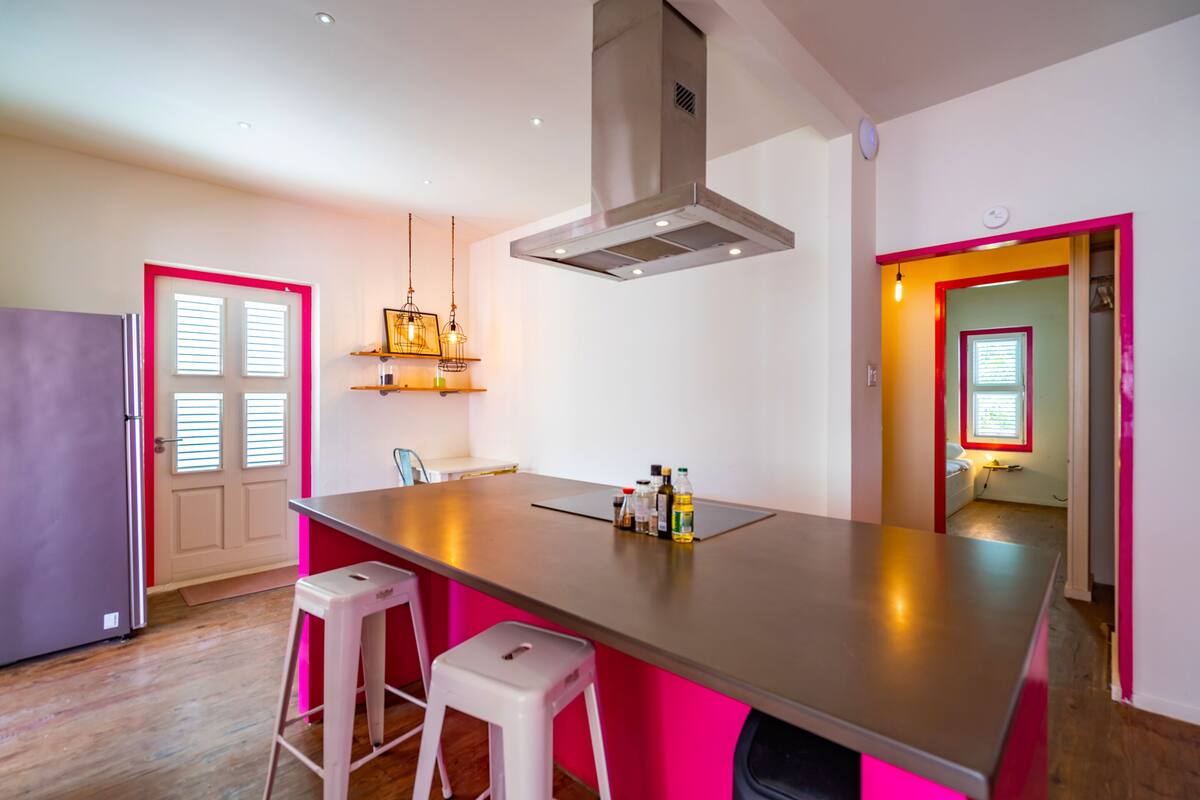 A modern kitchen with a central island, white bar stools, and pendant lighting.