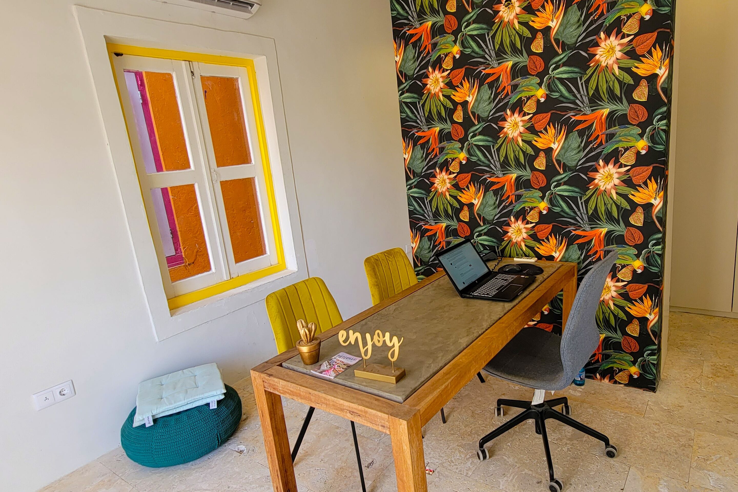Une salle de conférence avec une table en bois, deux chaises jaunes, un ordinateur portable et un panneau décoratif.