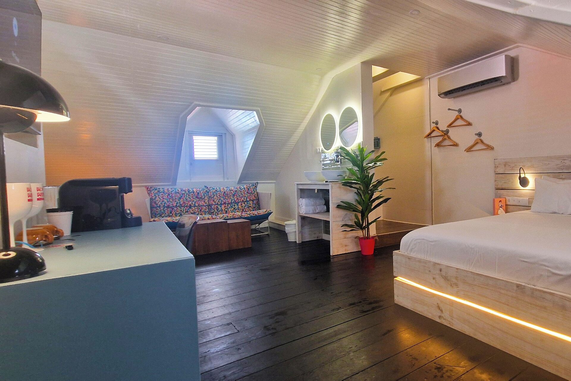 Un dormitorio moderno con cama, escritorio, silla, sofá y una planta en maceta.