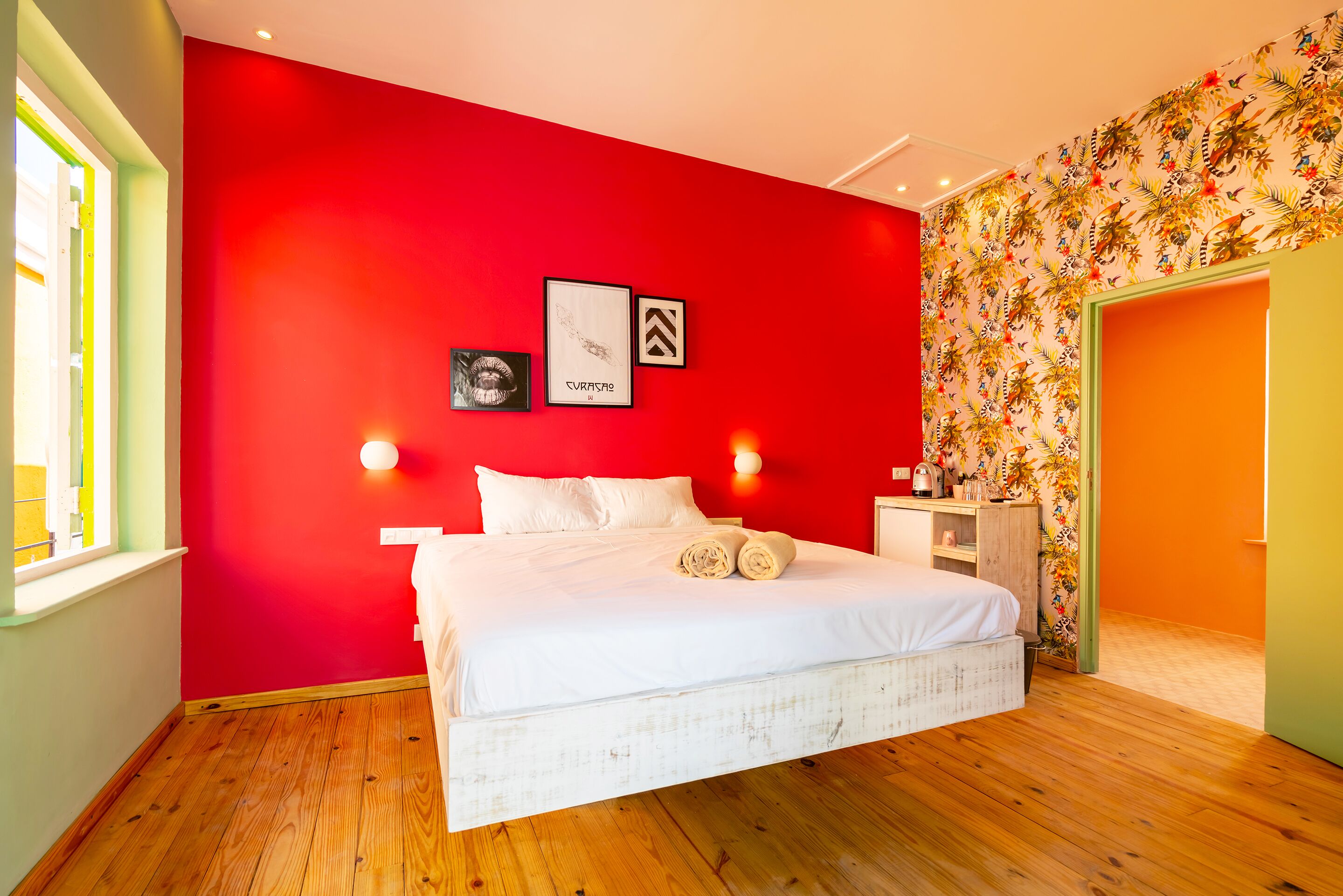 A bedroom with a red wall, a white bed, and a wooden floor.