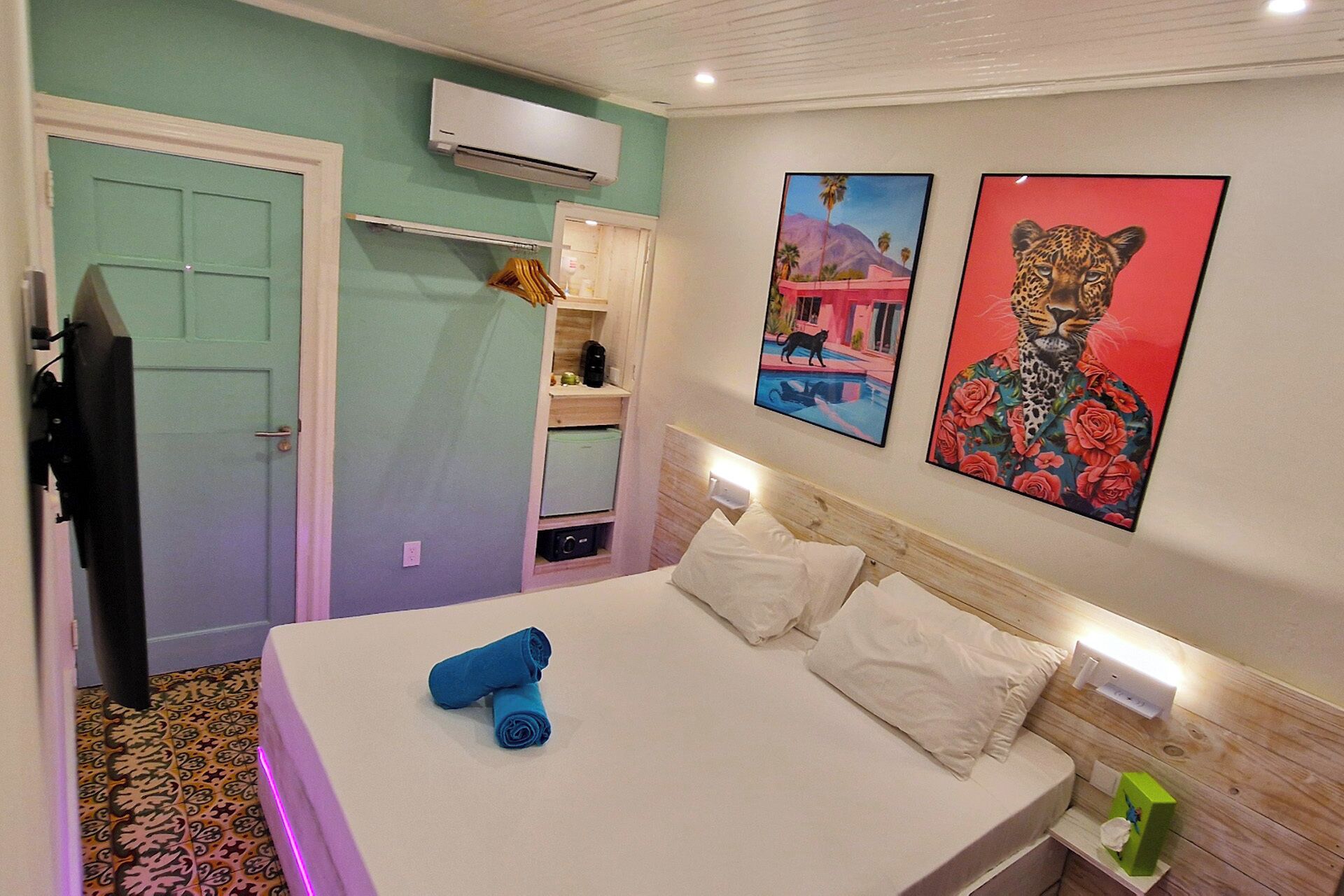 A hotel room with a bed, a small desk, a mirror, and artwork on the wall.