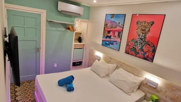 A hotel room with a bed, a small desk, a mirror, and artwork on the wall.