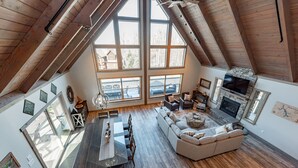 A spacious loft with a high ceiling, large windows, a dining area, a living room with a fireplace, and a stone fireplace.