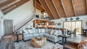 A spacious living area with a large L-shaped sectional sofa, a wooden coffee table, and a staircase leading to an upper level.