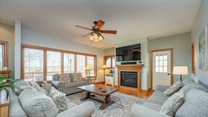 A living room with a fireplace, two sofas, a coffee table, and a ceiling fan. - Hot Tub, Fire Pit & Theater Room by Deep Creek (McHenry)