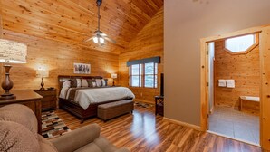 A wooden cabin bedroom with a bed, nightstands, a ceiling fan, and a view of the outside through a window.