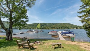 A lakeside dock with boats, a picnic area, and a forested hill in the background.