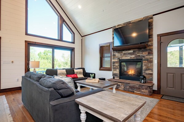 A living room with a stone fireplace, a large TV, and a cozy seating area. - Charming Dog Friendly Lake Area Home w/ Hot Tub (Oakland)