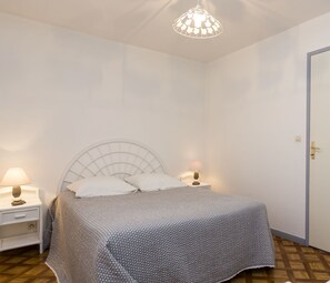 Quarto com uma cama, duas mesas de cabeceira, um criado-mudo, uma porta e um lustre.