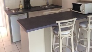 A compact kitchen with white cabinets, a black countertop, a sink, a coffee maker, a microwave, and two bar stools. - Duplex 4 pers lakeside, beach and bike path (biscarrosse)
