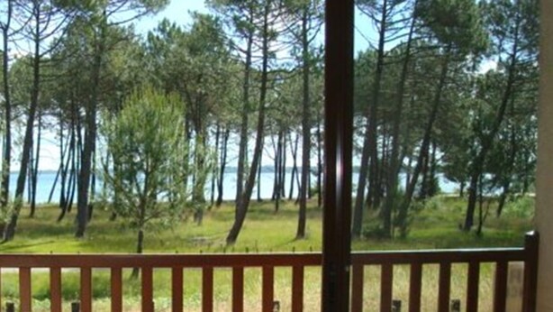 A wooden deck with two chairs and a table, overlooking a forest and a body of water. - Duplex 4 pers lakeside, beach and bike path (biscarrosse)