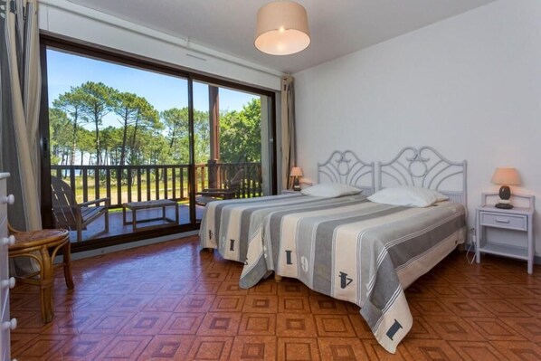 Quarto com duas camas, varanda e vista para árvores.