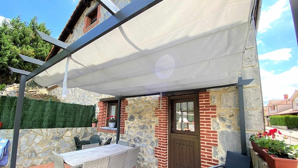 A patio area with a table and chairs, a covered seating area, and a stone wall. - Las Hortensias Country House in Hoznayo (Santa Marina (Entrambasaguas))