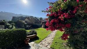 Ein Gartenweg führt zu einem Haus mit einem Stehendach und üppiger Bepflanzung.