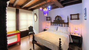 A bedroom with a wooden ceiling, a bed with a decorative headboard, bedside lamps, and a small table with a chair. - House (Llanes)
