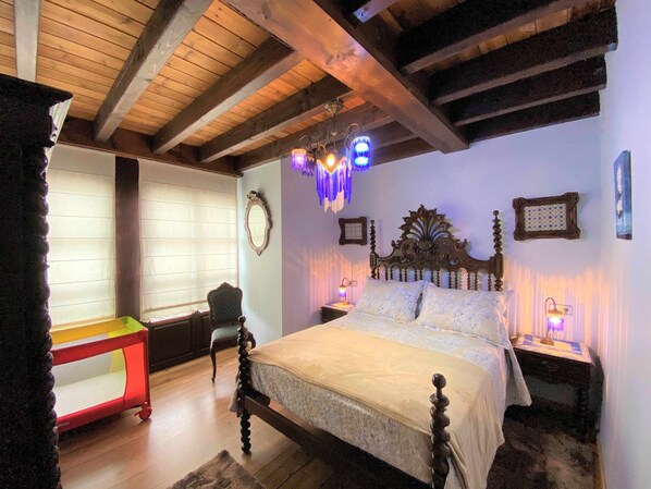 A bedroom with a wooden ceiling, a bed with a decorative headboard, bedside lamps, and a small table with a chair.