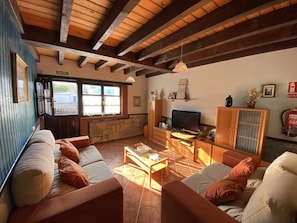 A cozy living room with a stone wall, wooden beams, a television, and a fireplace.