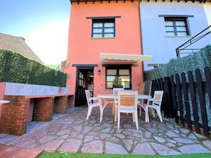 A patio with a brick barbecue area, a table with chairs, and a covered seating area with a striped awning.