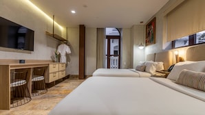 A hotel room with two beds, a desk with chairs, a TV, and a painting on the wall. - Hotel Voilá Centro Histórico (Cartagena)