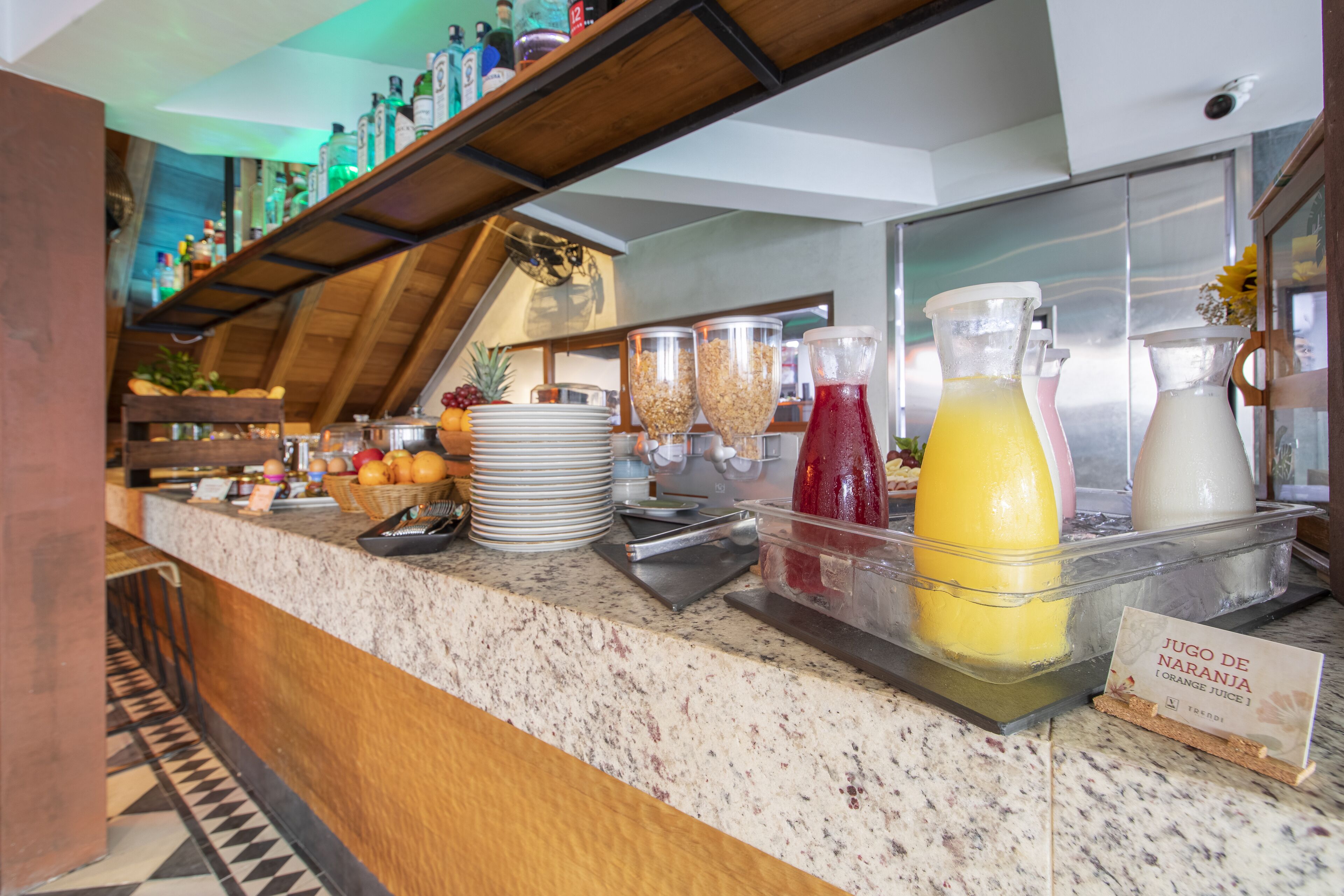A breakfast bar with various food items and beverages, including a sign for 'Jugo de Naranja'.