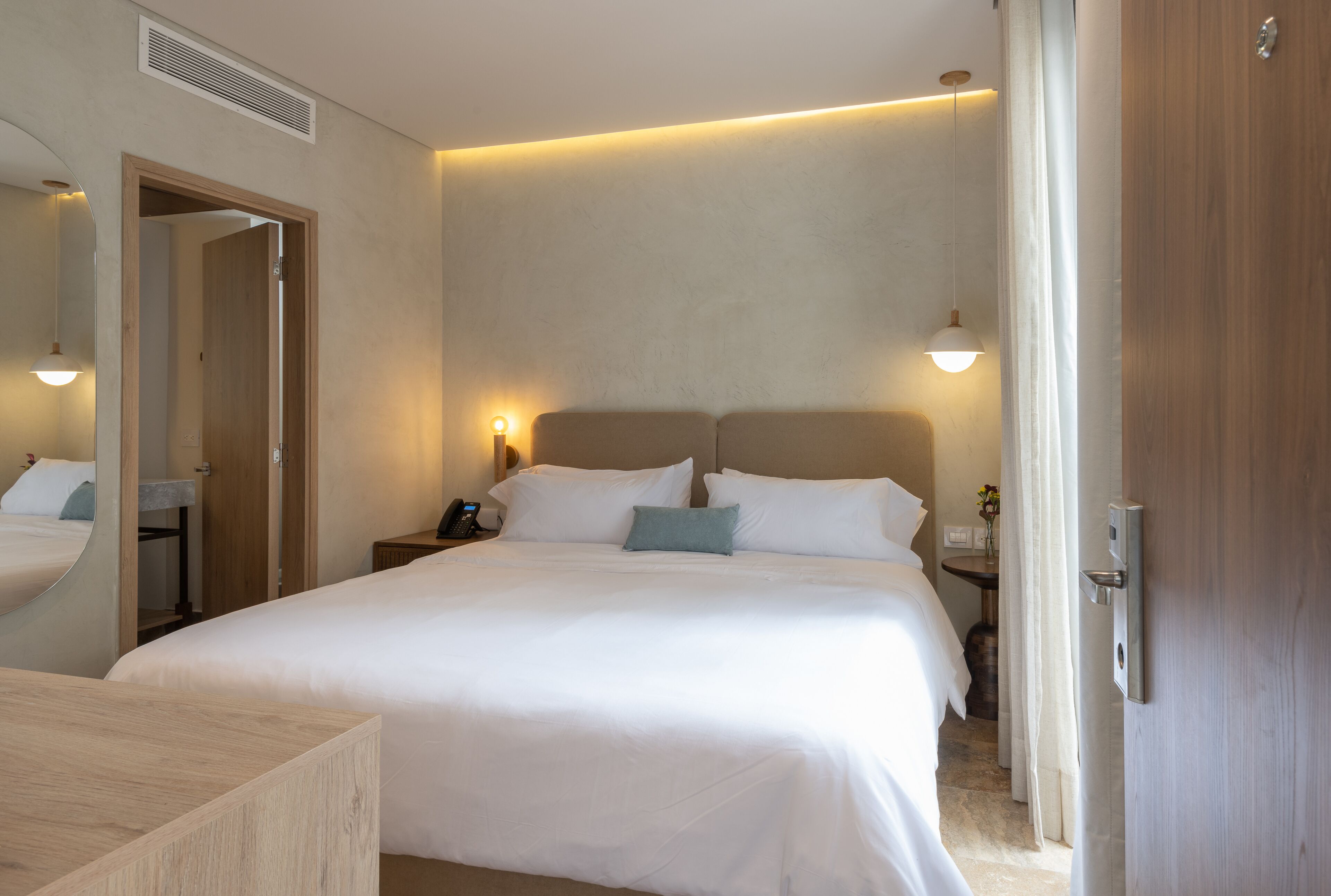 A hotel room with a large bed, bedside tables, a mirror, and a door.