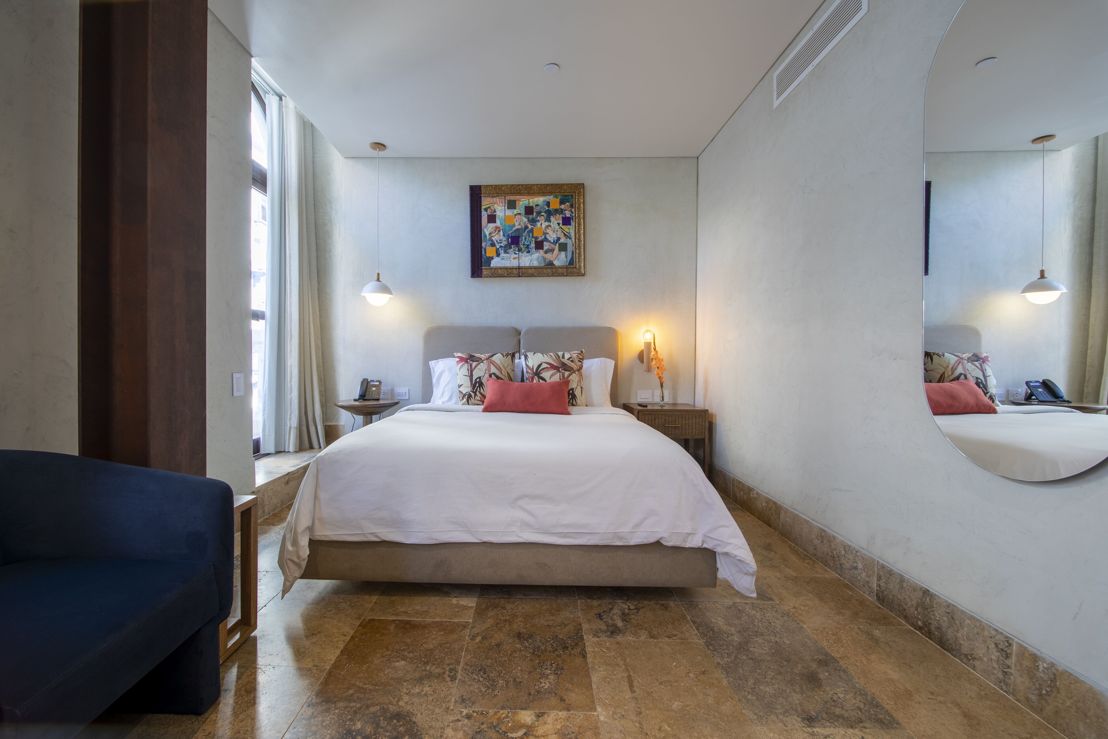 A bedroom with a large bed, a sofa, a nightstand, a lamp, and a painting on the wall.