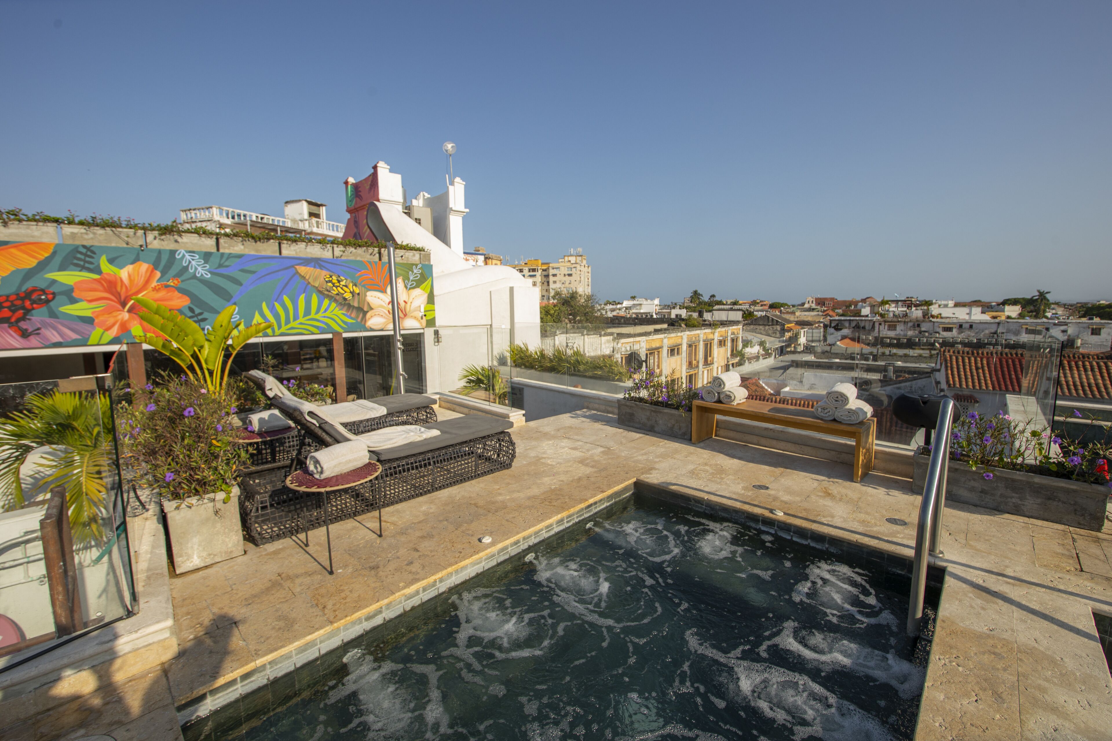 A rooftop pool area with lounge chairs, a hot tub, and a mural.