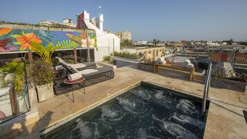 A rooftop pool area with lounge chairs, a hot tub, and a mural.