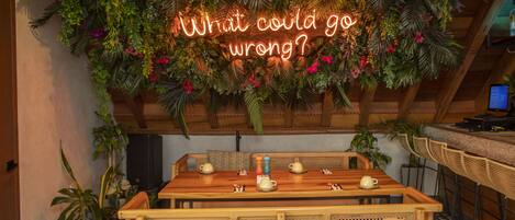 A cozy dining area with a wooden table, wicker chairs, and a neon sign above.