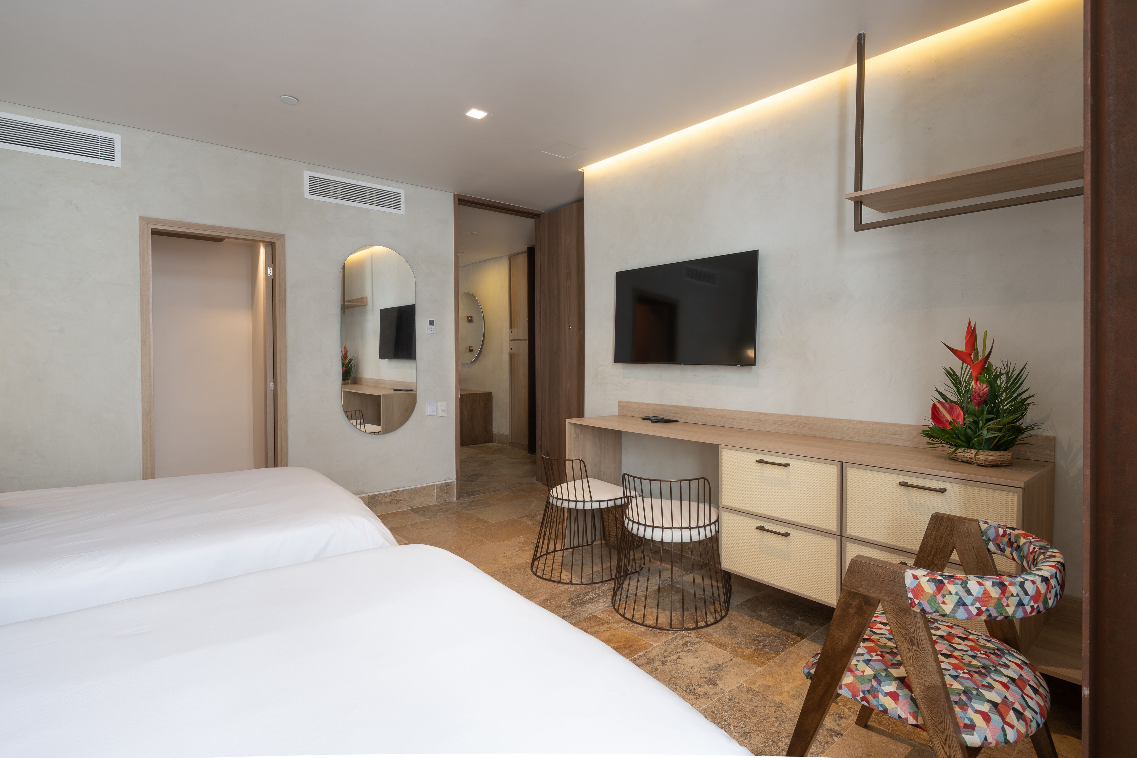 A modern hotel room with two beds, a desk with a chair, a TV, and a small plant.