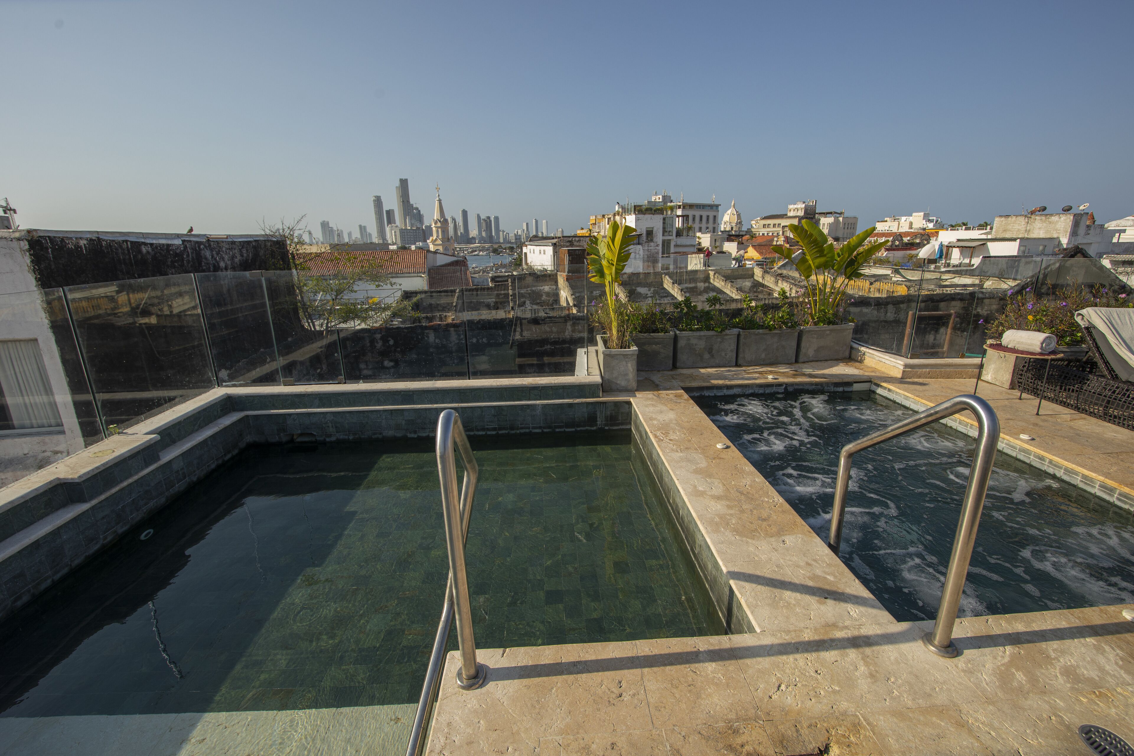A rooftop swimming pool with clear water, metal railings, and potted plants.
