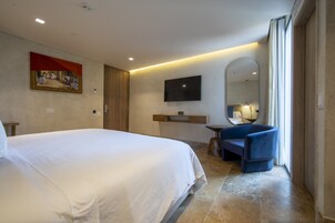 A hotel room with a large bed, a flat-screen TV mounted on the wall, a small table, and a blue armchair.