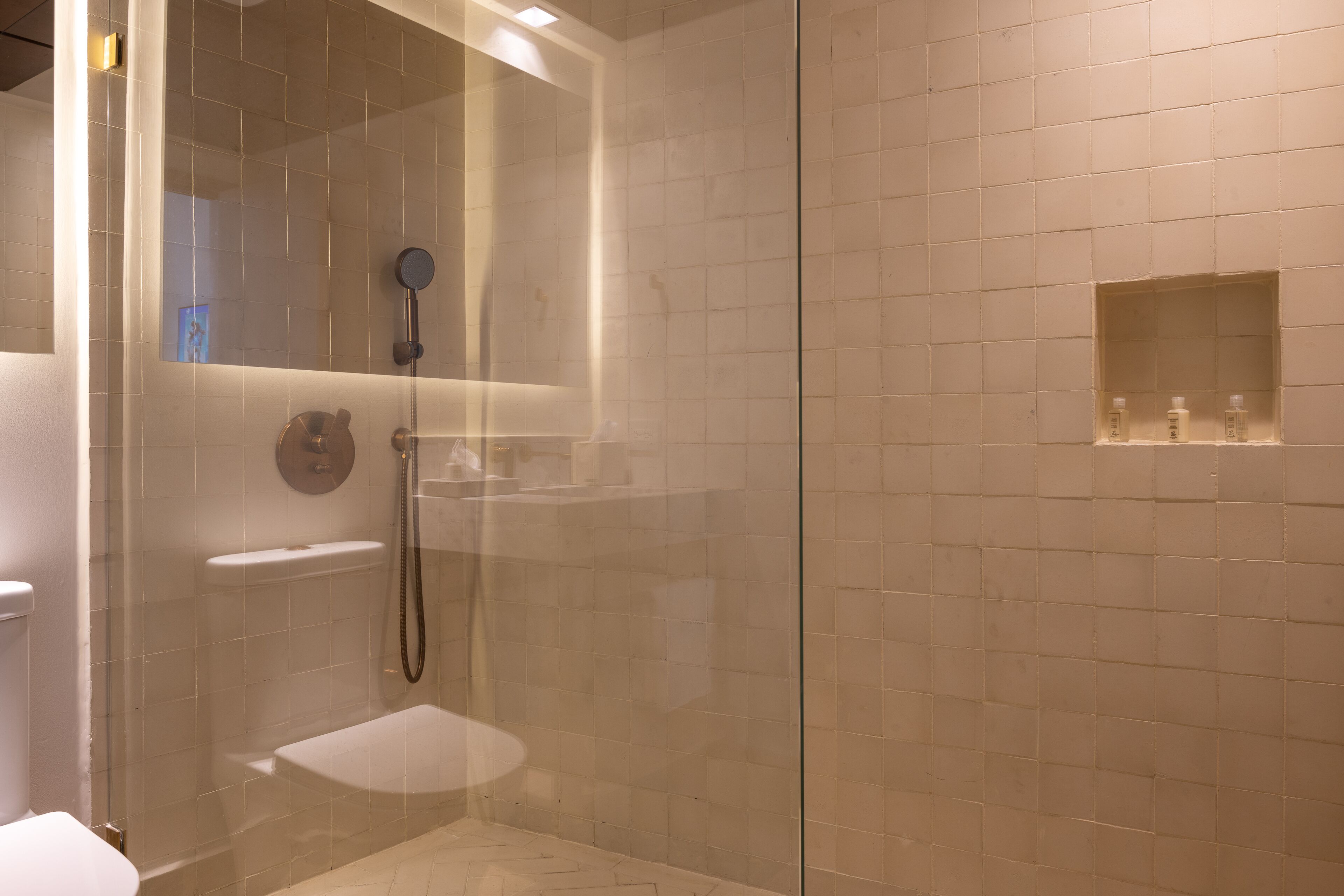 Un baño moderno con ducha de vidrio, inodoro y estante con artículos de tocador.