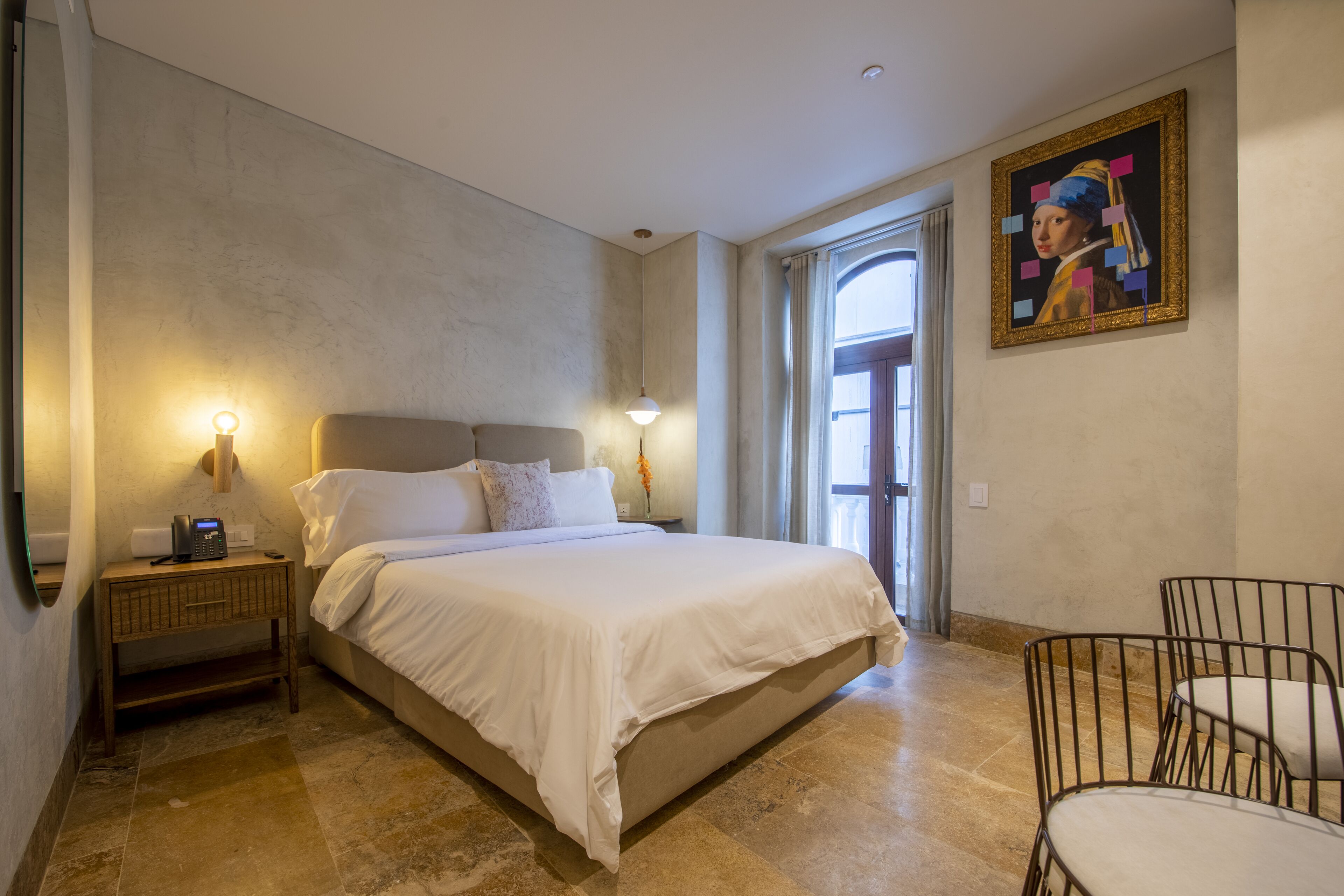 Un dormitorio con una cama grande, lámparas de noche, una mesita de noche, una silla y un cuadro en la pared.