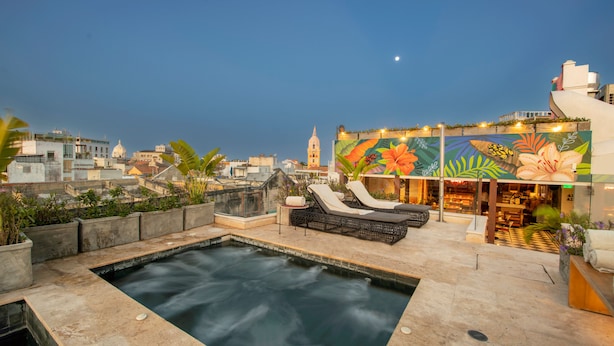 A rooftop pool area with lounge chairs and a hot tub, surrounded by city buildings and a mural. - Hotel Voilá Centro Histórico (Cartagena)