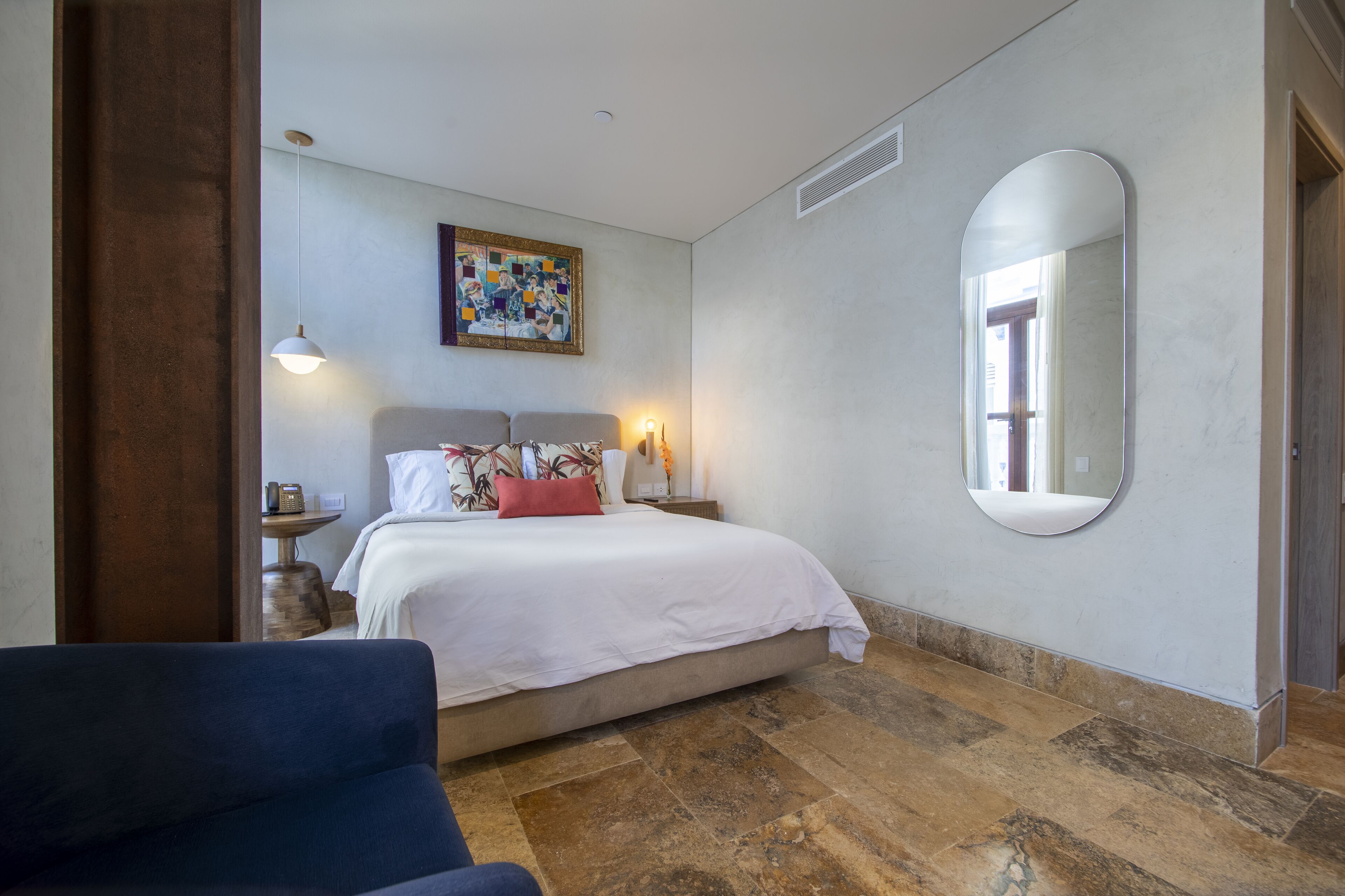 Un dormitorio con cama, un espejo redondo, un cuadro y una mesita de noche con lámpara.