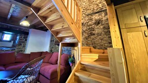Una scala in legno conduce a una zona mansardata con una parete in pietra, un divano rosso e una piccola pianta.