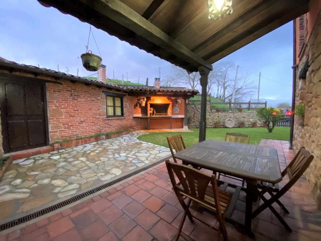 Un patio con suelo de losas de piedra, un edificio de ladrillo con chimenea y una zona de estar al aire libre cubierta con una mesa y sillas.