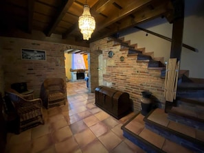 A cozy interior with a fireplace, wooden staircase, and wicker furniture.