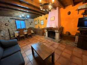 A cozy living room with a fireplace, stone walls, wooden furniture, and a television.