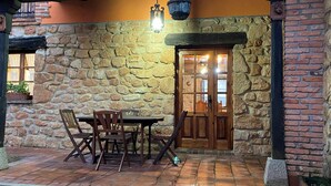 Eine Terrasse mit Steinplatten, einem Holztisch und Stühlen, einer Tür mit Glasscheiben und einem hängenden Laternenleuchter.