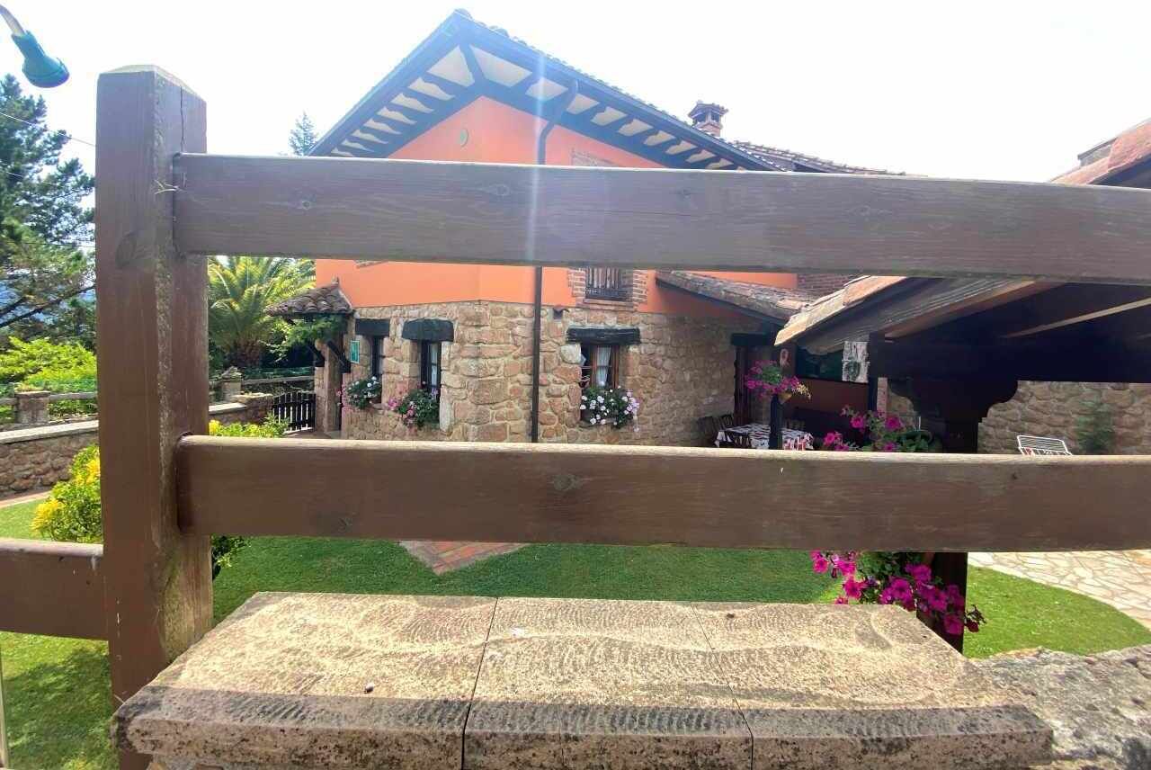 Un banc en bois se trouve devant un bâtiment en pierre, doté d’un toit en pente et de jardinières fleuries.