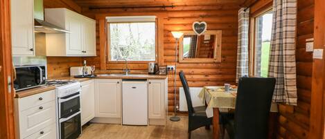A compact kitchen with white cabinets, a microwave, a stove, and a sink. There's a dining area with a table and chairs, and a window with a view of greenery.
