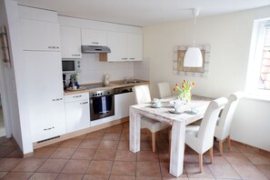 Une cuisine moderne avec des armoires blanches, un four encastré et une table à manger pour quatre personnes.