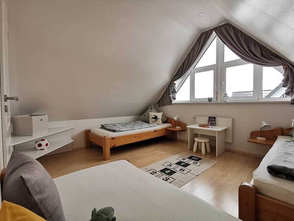Une pièce compacte et bien éclairée, avec un plafond en pente, un lit, un bureau et une fenêtre avec des rideaux.