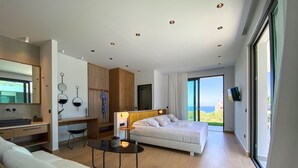 A modern hotel room with a bed, a desk, a sofa, and a large window offering a view of the sea. - Villa Lydia ,two pools, indoor heated pool , sea view (Κίσσαμος)