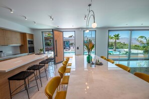A modern kitchen with a long island, bar stools, and a view of a pool and mountains.